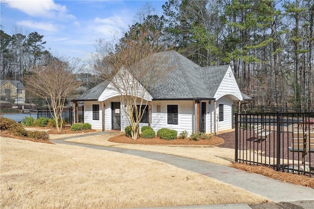 view of front facade with driveway, roof with shingles, and fence