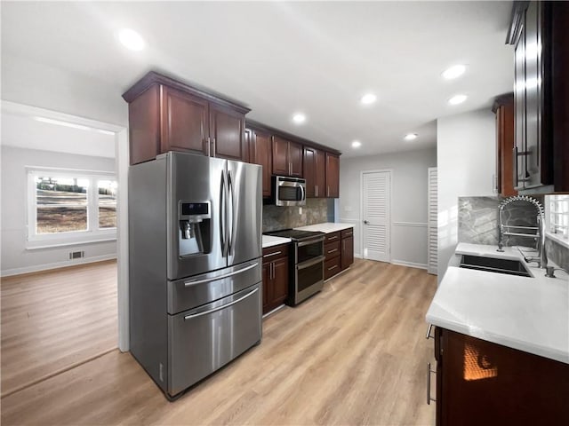 kitchen featuring dark brown cabinetry, sink, stainless steel appliances, light hardwood / wood-style floors, and backsplash