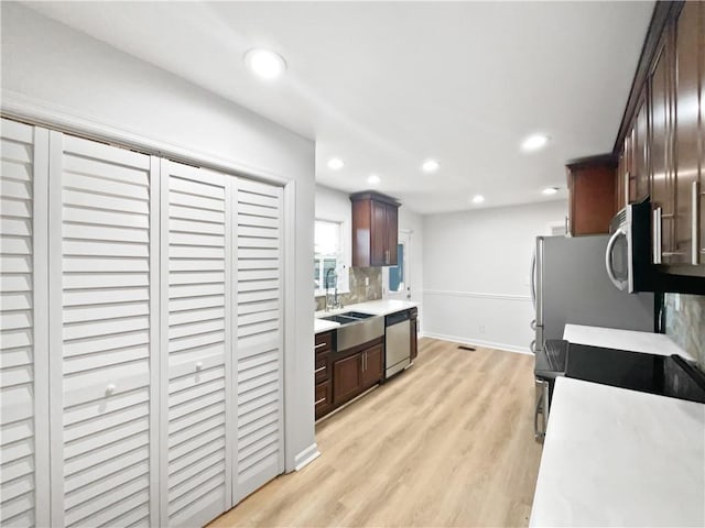 kitchen featuring stainless steel appliances, sink, light hardwood / wood-style floors, and decorative backsplash