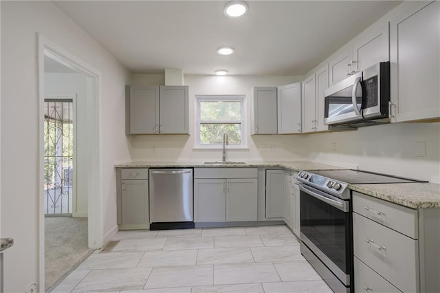 kitchen with gray cabinets, recessed lighting, light stone counters, stainless steel appliances, and a sink