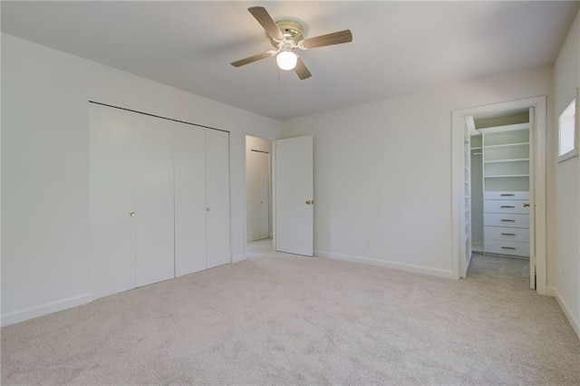 unfurnished bedroom with ceiling fan, a spacious closet, baseboards, and light carpet