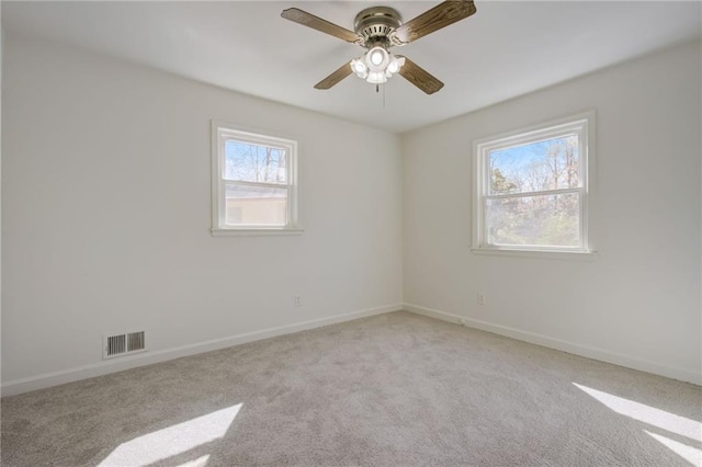 empty room with baseboards, visible vents, a ceiling fan, and light colored carpet