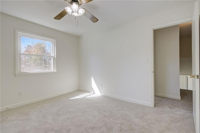 carpeted spare room featuring baseboards and a ceiling fan
