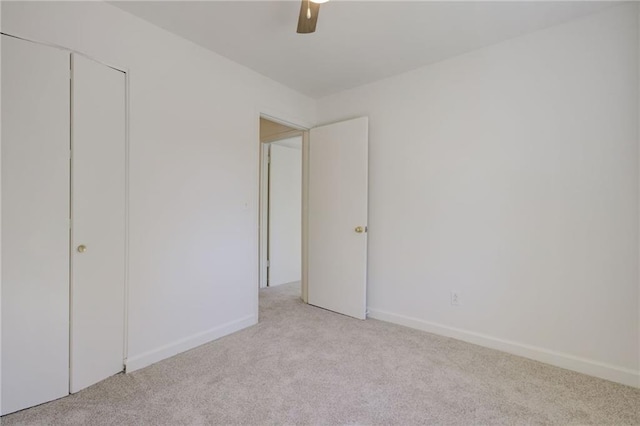 unfurnished bedroom featuring baseboards, ceiling fan, a closet, and light colored carpet