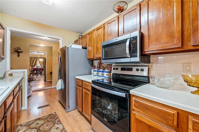 kitchen featuring decorative backsplash, brown cabinets, stainless steel appliances, light countertops, and light wood-style floors