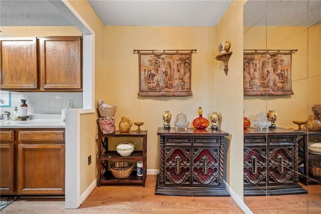 interior space with a textured ceiling, light wood finished floors, baseboards, and tasteful backsplash