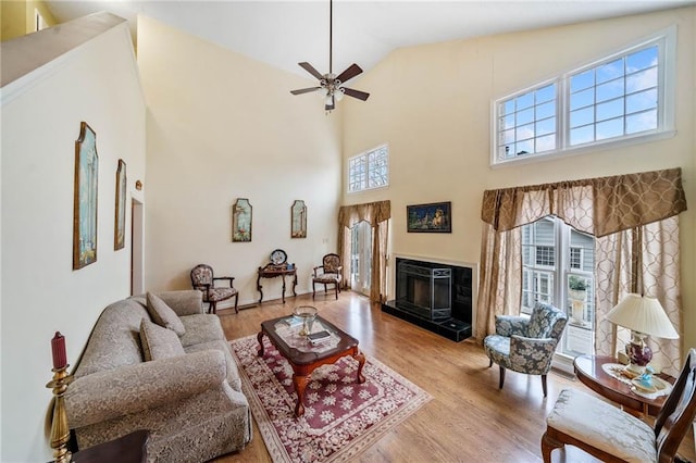 living room featuring ceiling fan, high vaulted ceiling, a glass covered fireplace, and light wood-style floors