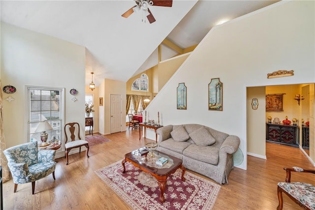 living area featuring baseboards, ceiling fan, stairs, light wood-type flooring, and high vaulted ceiling