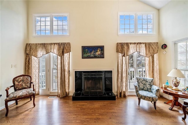 sitting room featuring a fireplace with raised hearth, a towering ceiling, and wood finished floors