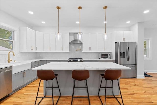 kitchen featuring light wood-type flooring, wall chimney exhaust hood, appliances with stainless steel finishes, and gray cabinetry