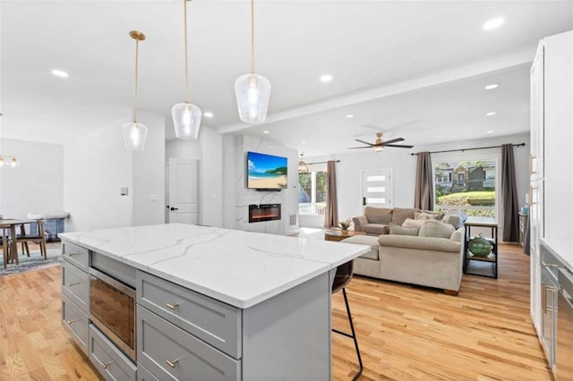 kitchen with a center island, gray cabinets, light wood-style flooring, a glass covered fireplace, and a kitchen bar