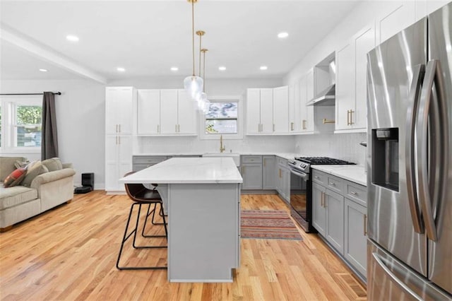 kitchen with decorative backsplash, appliances with stainless steel finishes, a breakfast bar area, gray cabinets, and light wood-type flooring