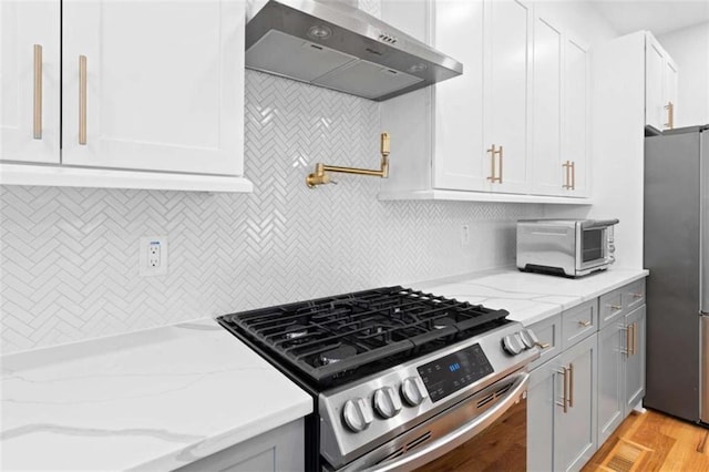 kitchen with extractor fan, a toaster, stainless steel appliances, white cabinets, and light stone countertops