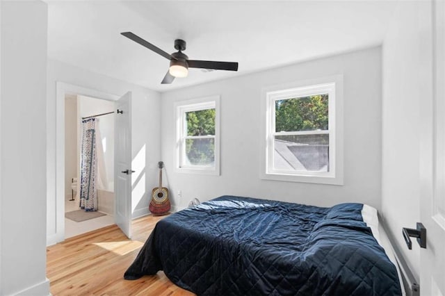 bedroom featuring a ceiling fan, ensuite bath, baseboards, and wood finished floors