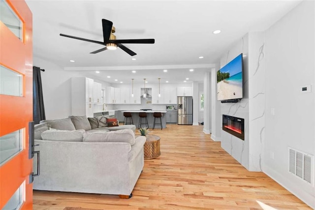 living area with recessed lighting, visible vents, light wood-style floors, a glass covered fireplace, and a ceiling fan