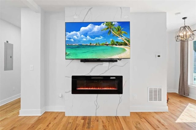 room details featuring wood finished floors, visible vents, electric panel, a glass covered fireplace, and an inviting chandelier