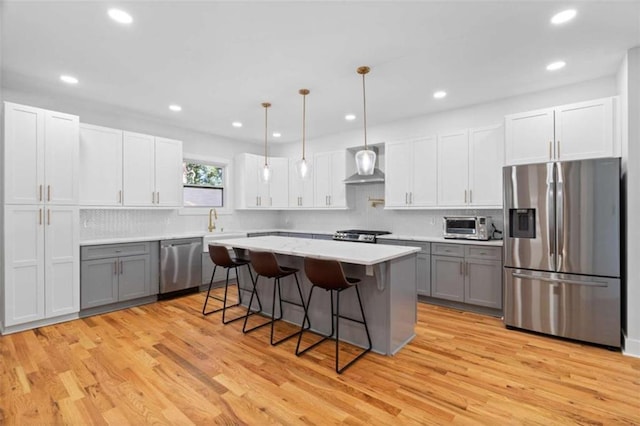 kitchen featuring light wood-style flooring, a kitchen breakfast bar, stainless steel appliances, light countertops, and wall chimney range hood