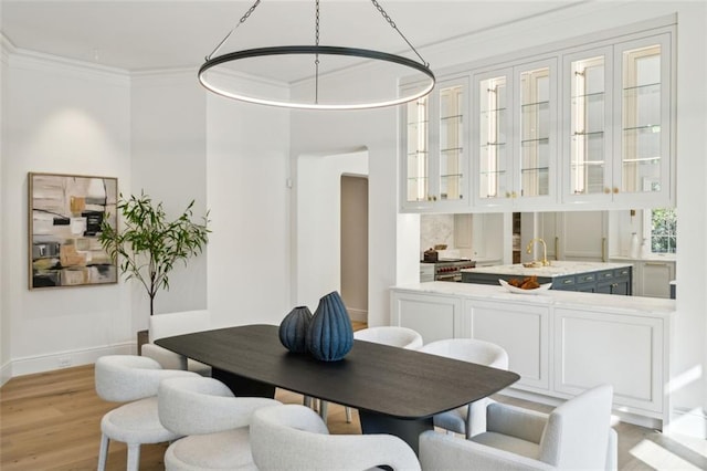 dining space with sink, light wood-type flooring, and crown molding