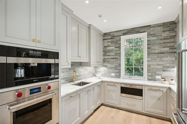 kitchen with sink, stainless steel appliances, tasteful backsplash, light stone counters, and light hardwood / wood-style floors