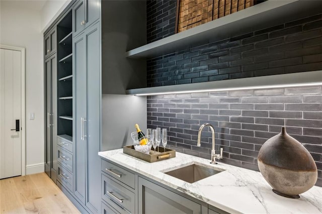 kitchen with tasteful backsplash, light stone counters, sink, and light wood-type flooring