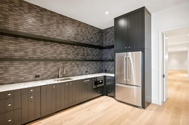 kitchen with light stone countertops, decorative backsplash, high quality fridge, sink, and light hardwood / wood-style floors