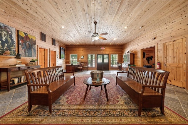 living area with ceiling fan, wooden ceiling, and wooden walls