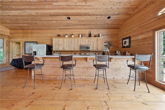 kitchen with light hardwood / wood-style floors, vaulted ceiling, a kitchen bar, light brown cabinetry, and appliances with stainless steel finishes