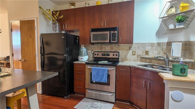 kitchen featuring light stone counters, a sink, stainless steel appliances, dark wood-type flooring, and tasteful backsplash