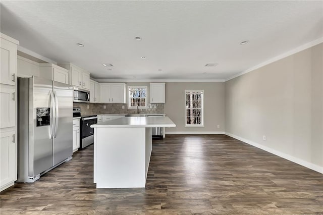 kitchen featuring appliances with stainless steel finishes, dark wood-type flooring, crown molding, white cabinets, and a kitchen island