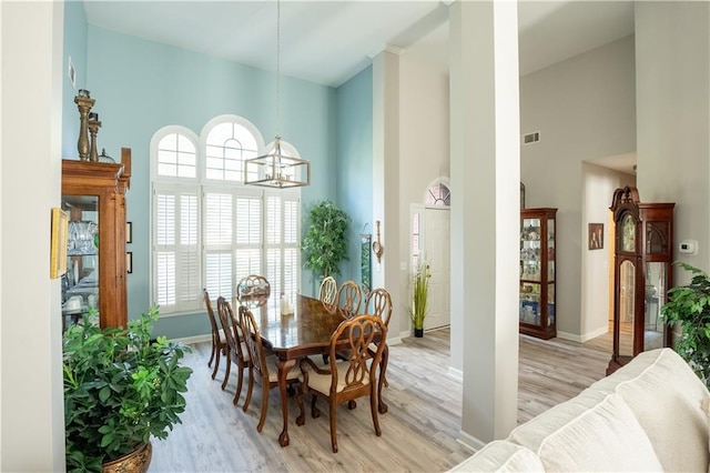 dining room with light wood-type flooring, a towering ceiling, and an inviting chandelier