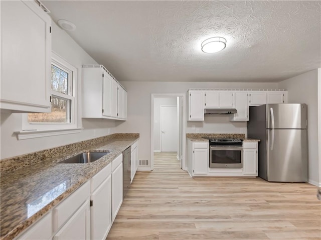 kitchen with stainless steel appliances, light stone countertops, white cabinets, and light hardwood / wood-style flooring