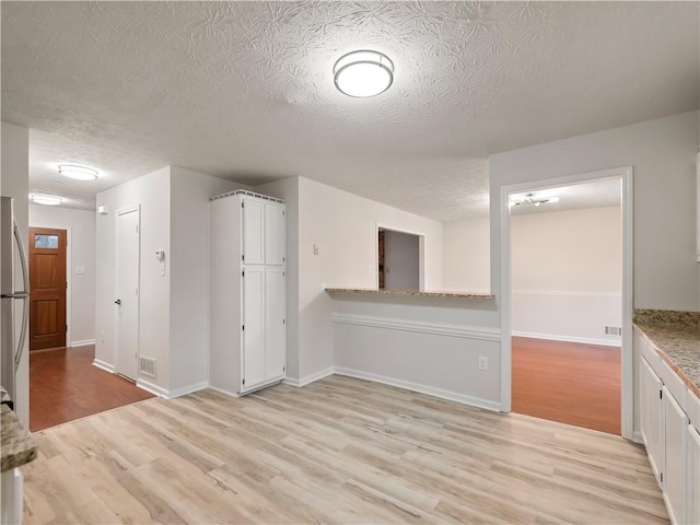 interior space with stainless steel fridge, white cabinetry, light stone countertops, light hardwood / wood-style floors, and a textured ceiling