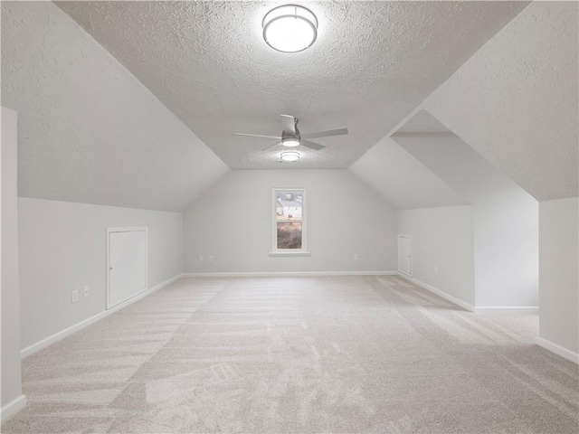 additional living space featuring light carpet, a textured ceiling, lofted ceiling, and ceiling fan