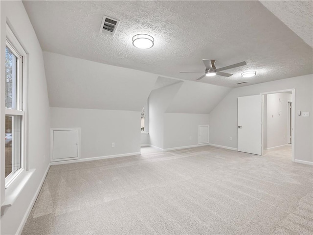 additional living space featuring vaulted ceiling, light colored carpet, ceiling fan, and a textured ceiling