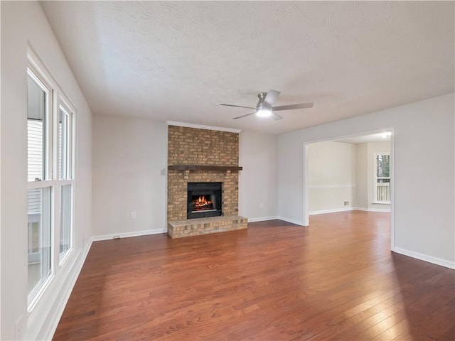 unfurnished living room featuring dark hardwood / wood-style flooring, a brick fireplace, a textured ceiling, and a healthy amount of sunlight