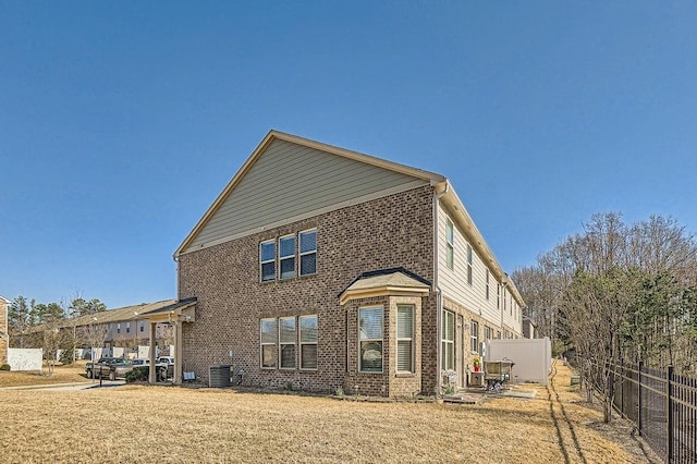 back of property featuring central air condition unit, brick siding, a lawn, and fence