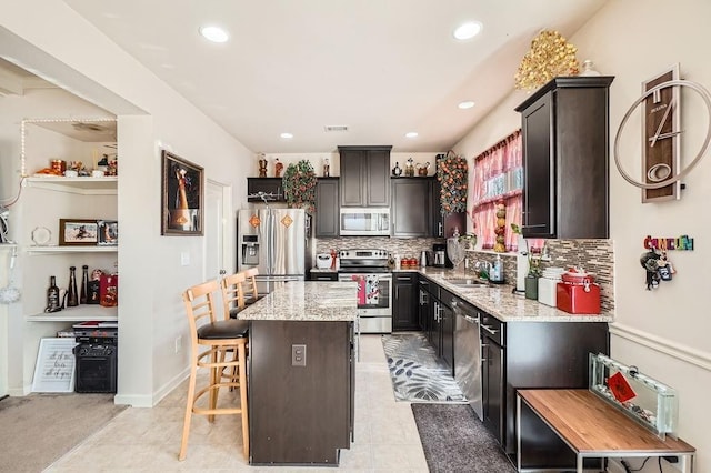 kitchen with tasteful backsplash, a kitchen island, light stone countertops, a kitchen breakfast bar, and stainless steel appliances