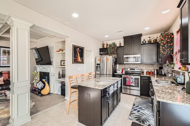 kitchen with a breakfast bar area, a kitchen island, a fireplace, a sink, and stainless steel appliances