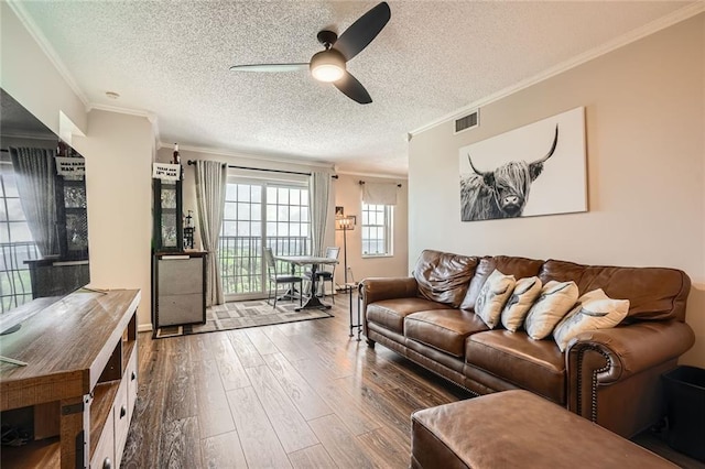 living area featuring visible vents, ornamental molding, wood finished floors, ceiling fan, and a textured ceiling
