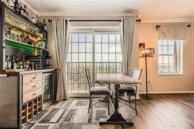 dining room with baseboards, wood finished floors, wine cooler, ornamental molding, and a bar