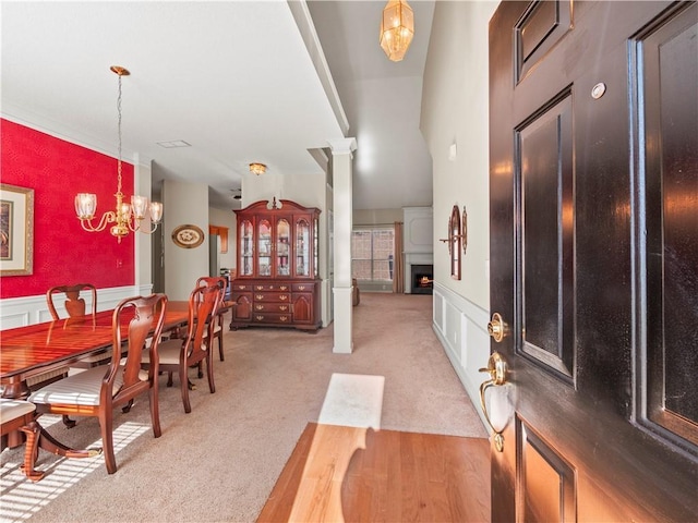 carpeted dining space featuring a large fireplace, decorative columns, and a notable chandelier