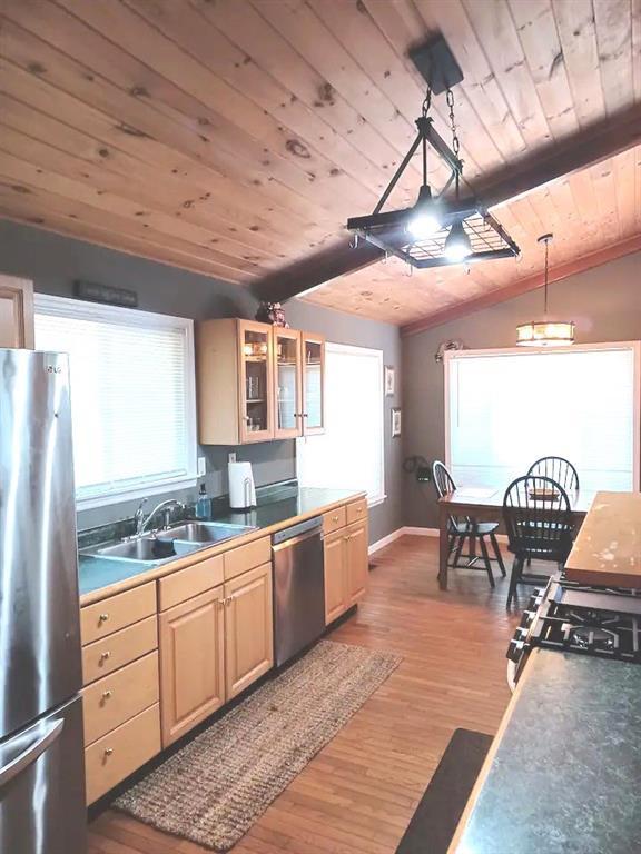 kitchen with lofted ceiling with beams, wood ceiling, appliances with stainless steel finishes, light wood-style floors, and a sink