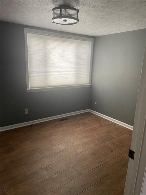 spare room featuring a wealth of natural light, dark wood-style flooring, and baseboards