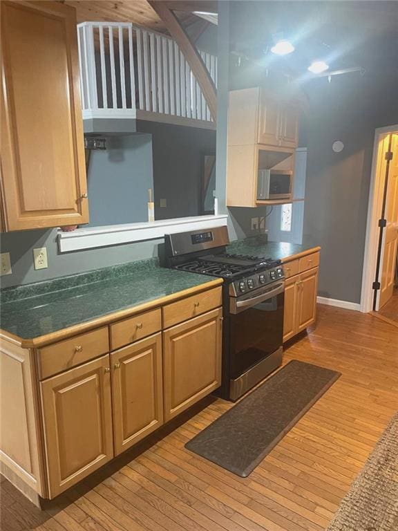 kitchen featuring light wood finished floors, a high ceiling, baseboards, and gas stove