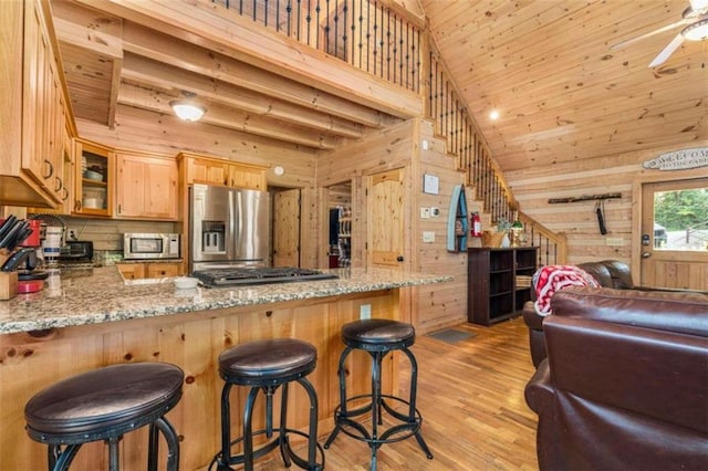 kitchen featuring appliances with stainless steel finishes, light stone counters, kitchen peninsula, wood walls, and high vaulted ceiling