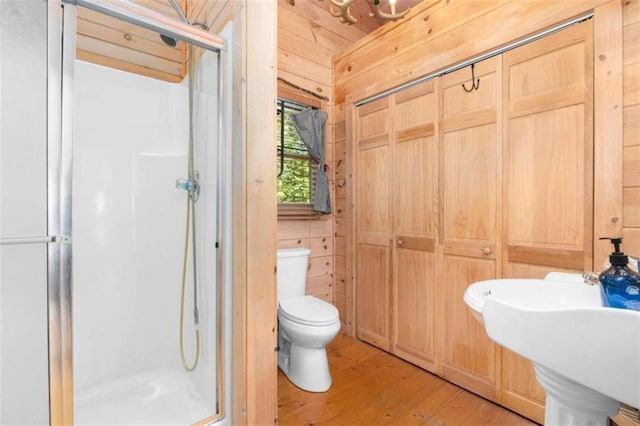 bathroom with hardwood / wood-style floors, walk in shower, toilet, and wood walls