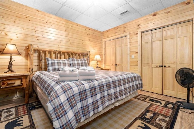 bedroom featuring multiple closets, a paneled ceiling, wooden walls, and light hardwood / wood-style floors