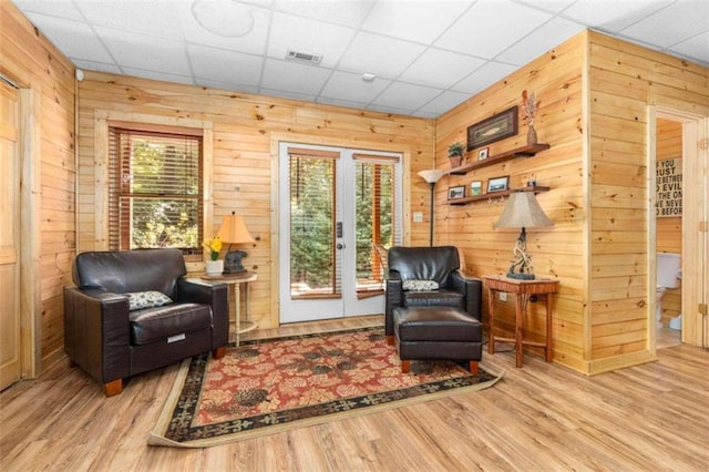 living area with plenty of natural light, a paneled ceiling, light wood-type flooring, and wooden walls