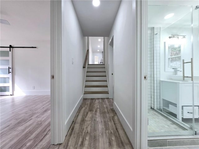 hall with stairs, a barn door, wood finished floors, and baseboards