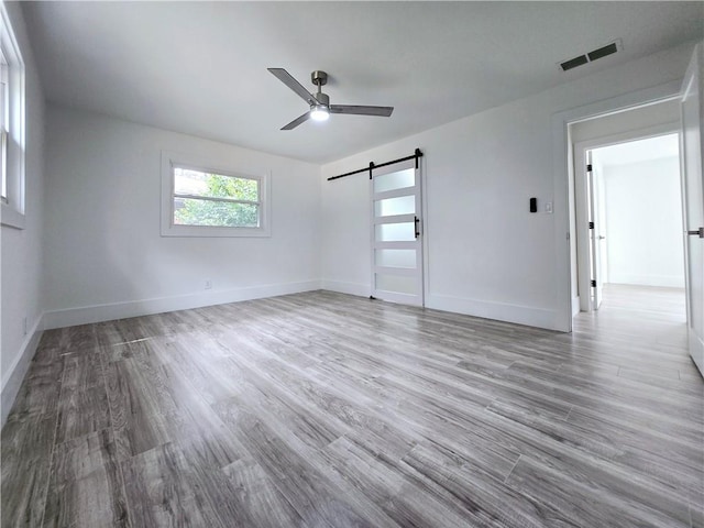 empty room featuring ceiling fan, baseboards, a barn door, and wood finished floors